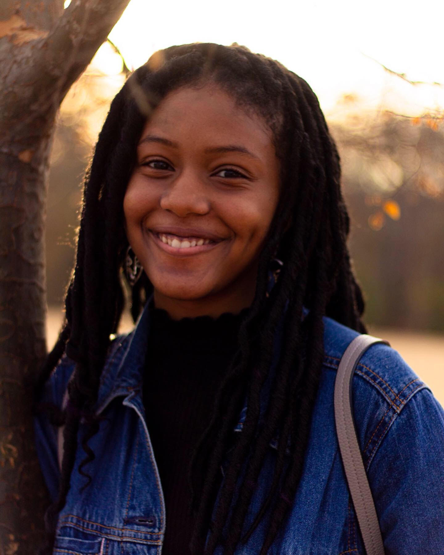 Nia Wright with dark brown locs and a jean jacket at sunset